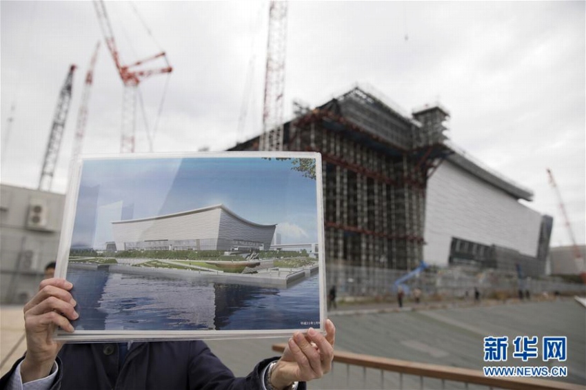 2月12日、東京「有明アリーナ」の建設現場で、完成予想図を手にする関係者。バレーボール競技とパラリンピックの車いすバスケットボールの試合がここで行われる計畫。1月末の時點で51％が完成している（撮影?杜瀟逸）。 