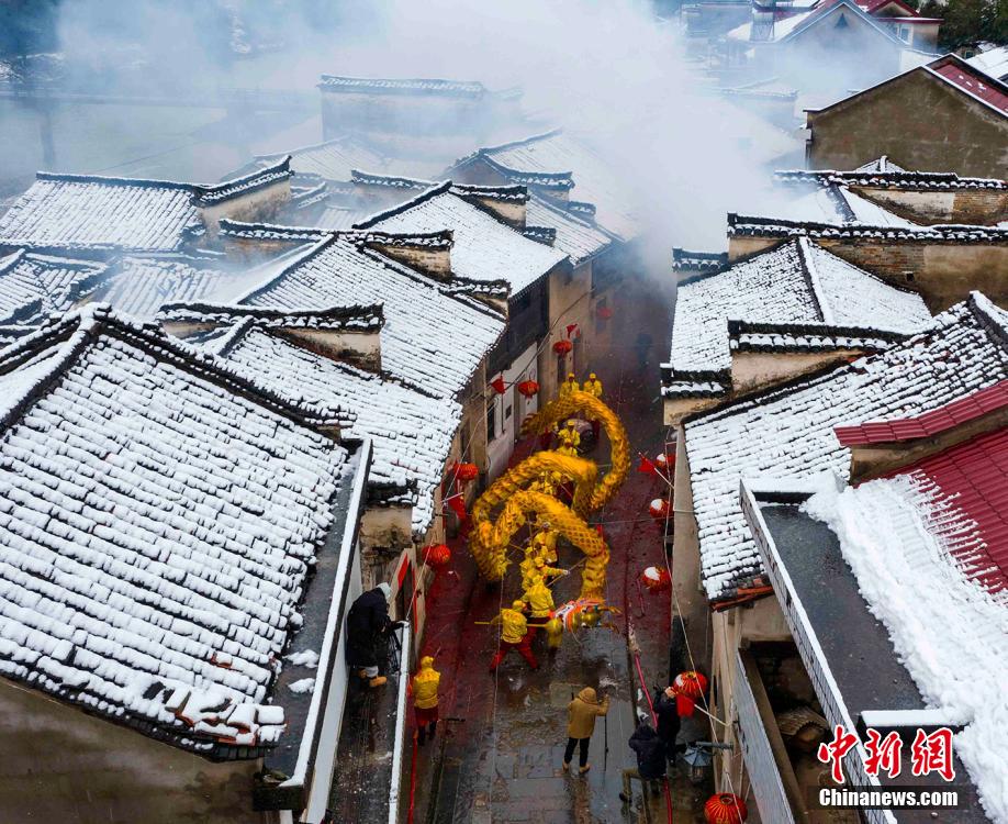 安徽省寧國市胡楽鎮で、雪が積もった歴史ある通りを胡楽司龍燈チームが元宵節の龍の舞いを披露しながらねり歩く様子（2月14日撮影?李暁紅）。